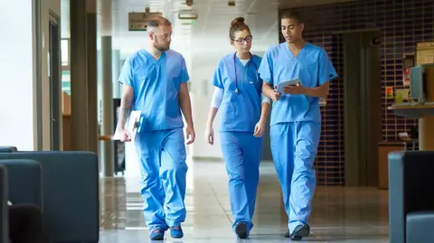 Getty Images Three junior doctors walking down a hospital corridor while wearing blue scrubs
