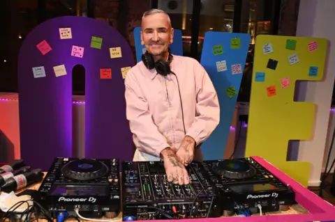 Getty Images DJ Fat Tony in a pink shirt smiling while on the decks