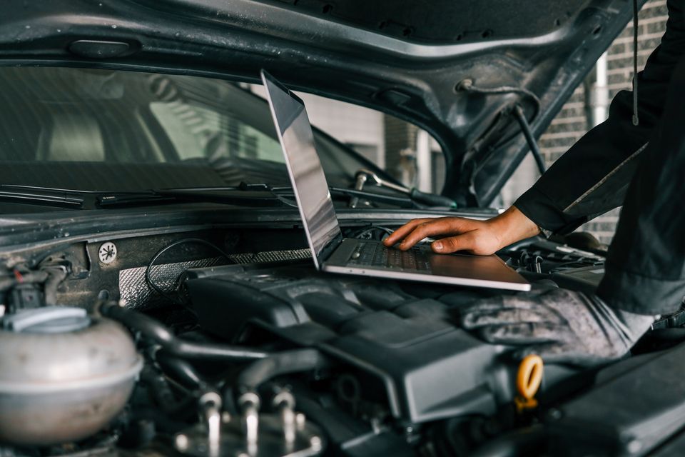 A mechanic uses a laptop for a diagnostics check on a car engine