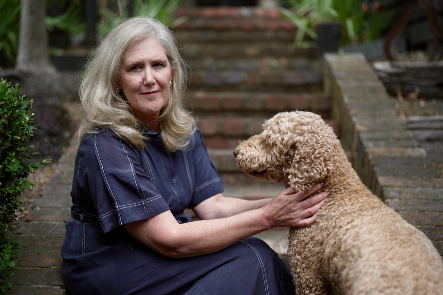 A woman with blonde hair sits on steps with her dog by her side