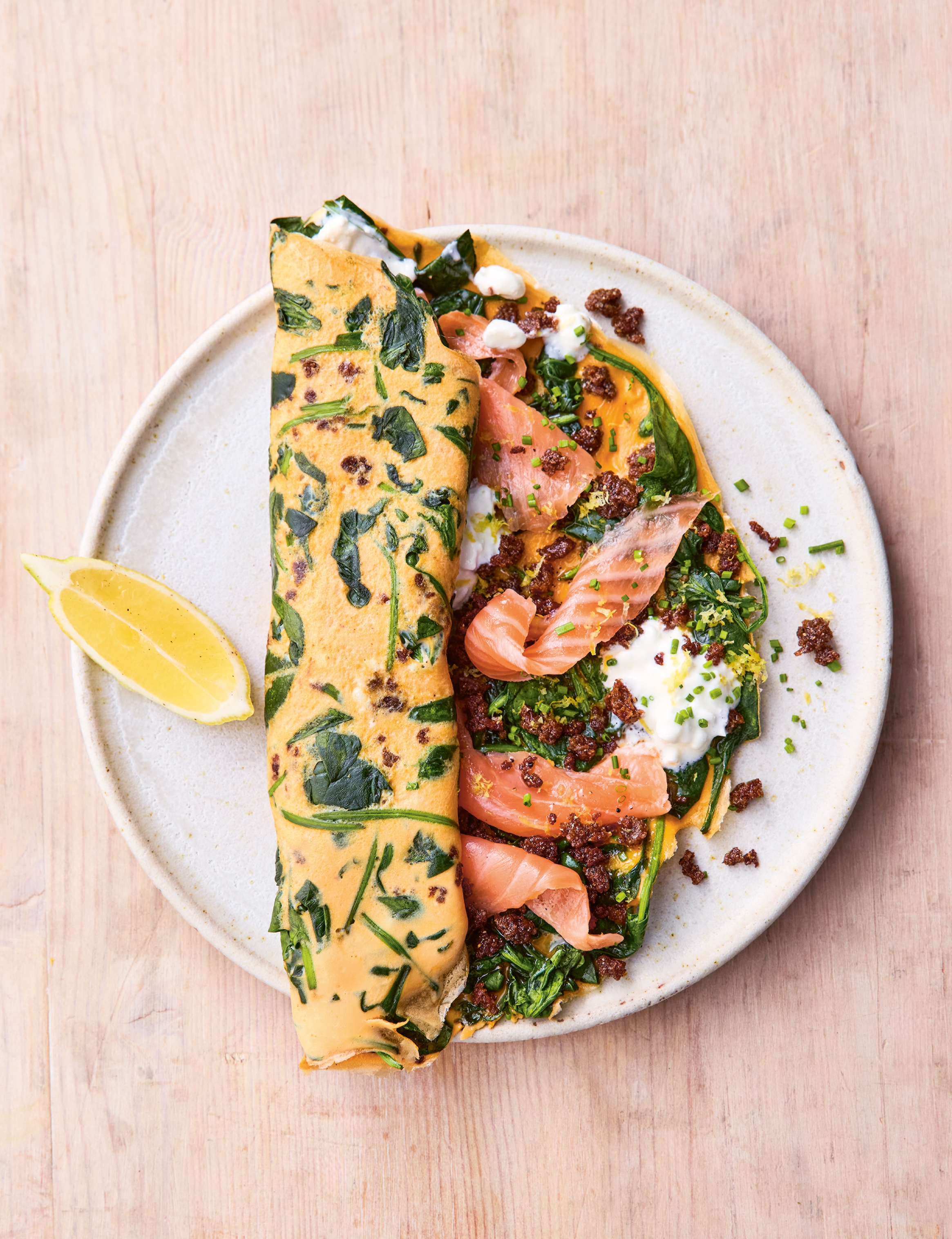 A smoked salmon and rye bread omelette on a white plate with a wedge of lemon