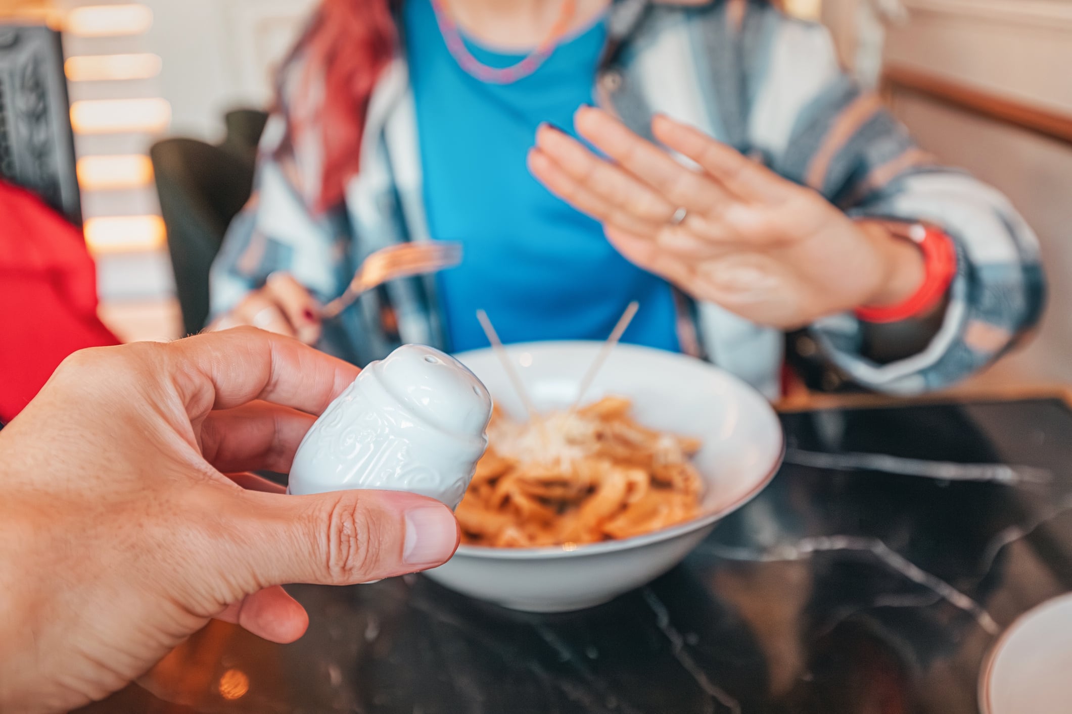 Hand holding salt shaker near plate of pasta and woman making refuse no gesture with hand in restaurant GettyImages-2214693183 frantic00.jpg