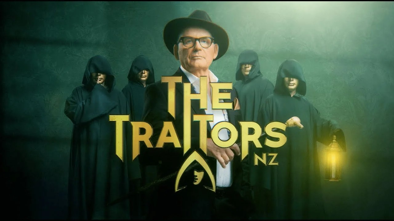 Host Paul Henry wearing a fedora and glasses stands at the center, surrounded by four figures in dark green hooded cloaks and gold masks.