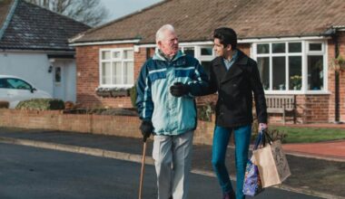 Teenage boy is walking back from the shop with his grandparent. He is carrying the shopping bag and they are linking arms.