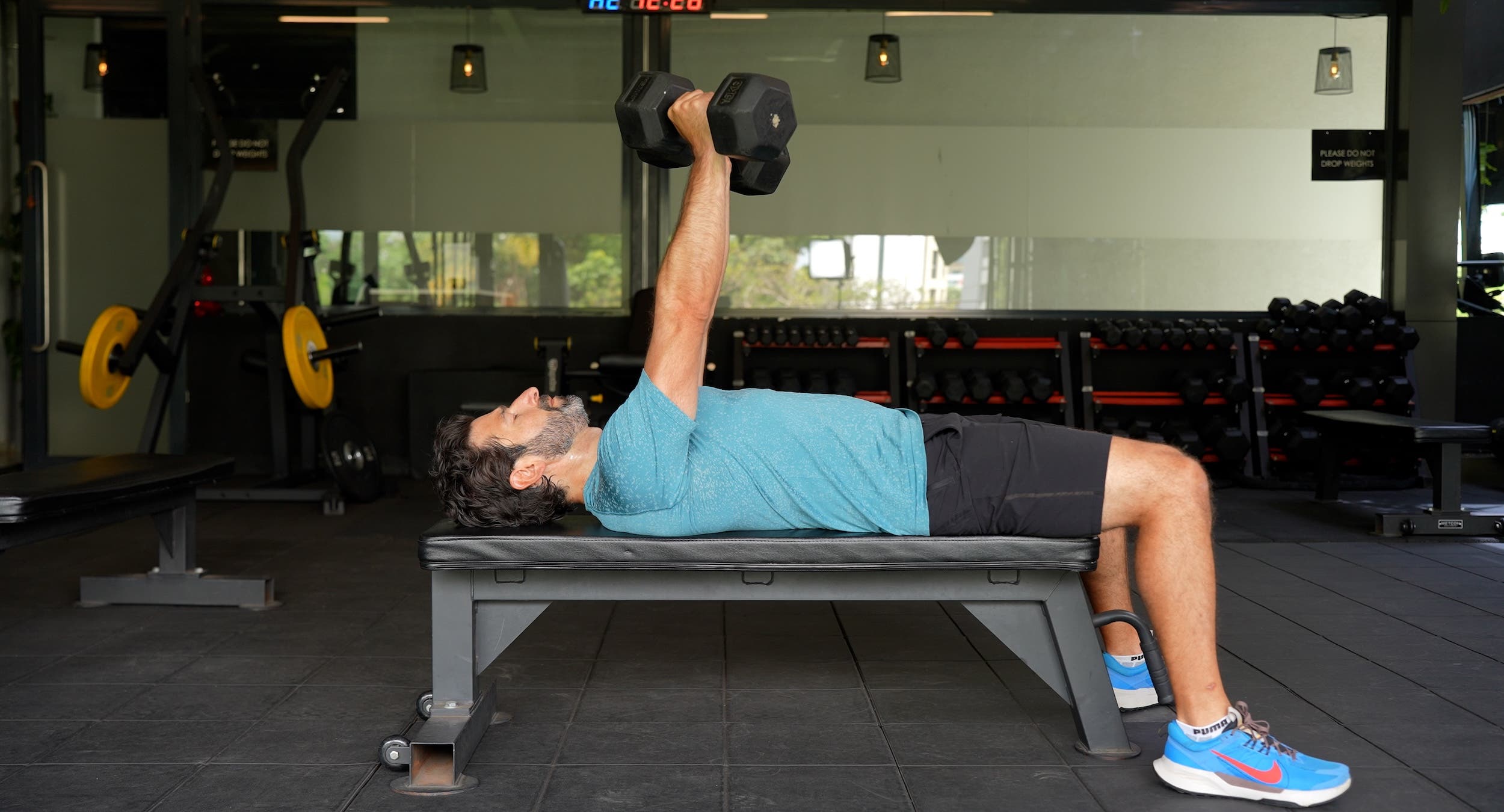 main with dark hair and a beard does a dumbbell bench press as part of a longevity workout plan