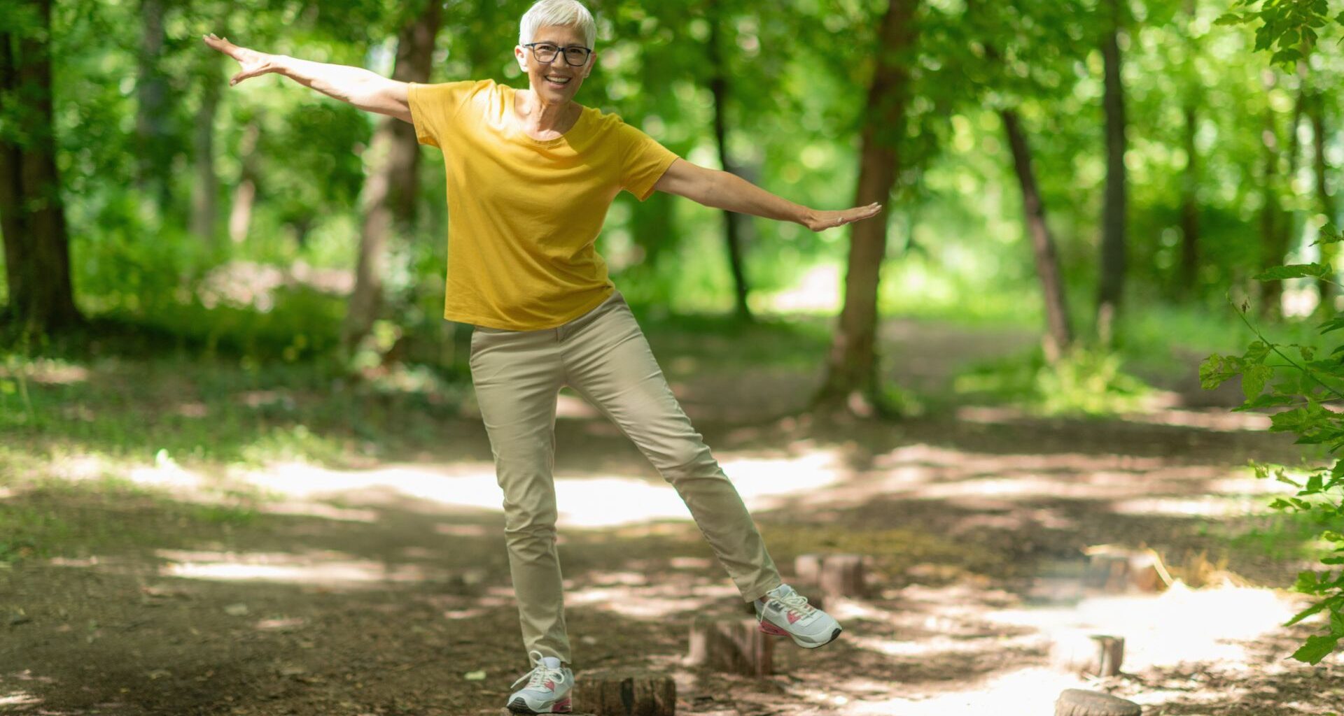 woman balances on one leg on tree stump