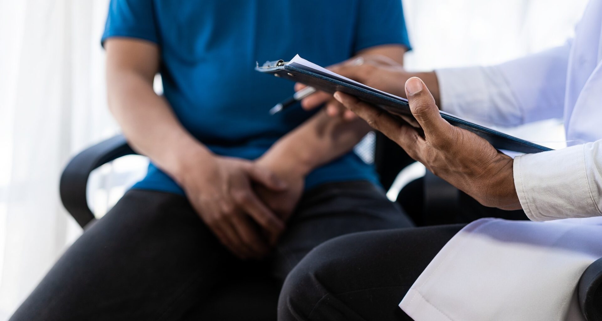Male patient sitting in doctors office. Man hands holding crotch area