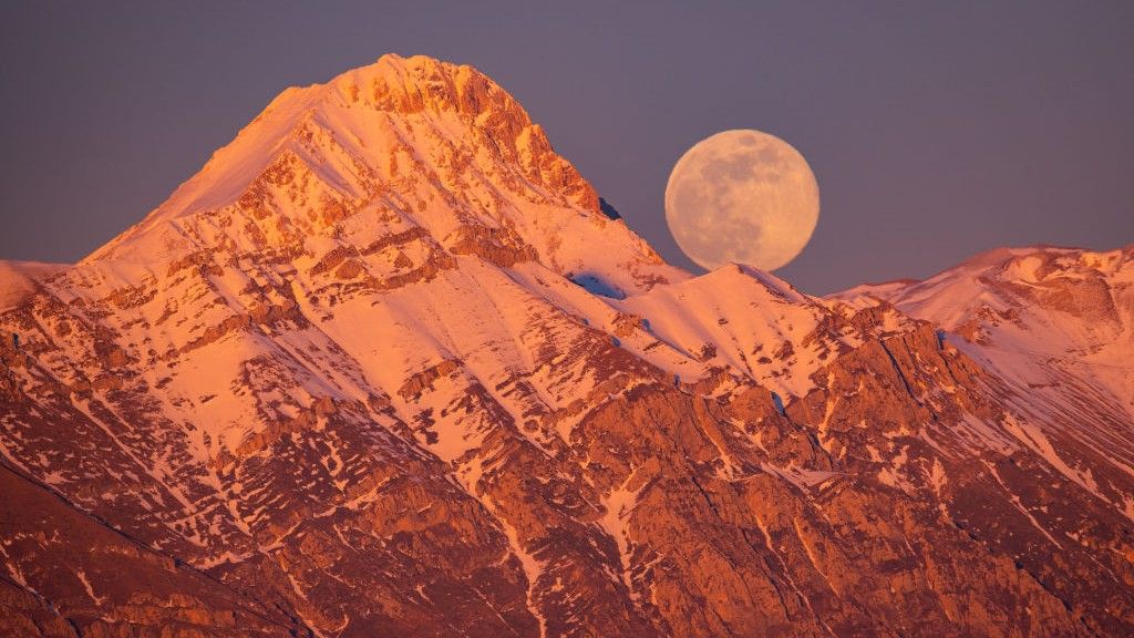 Wolf moon rising next to Corno Grande and Pizzo Cefalone peaks in Italy.