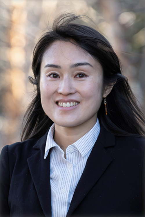 Smiling woman with dark hair wearing a dark blue blazer with striped dress shirt.