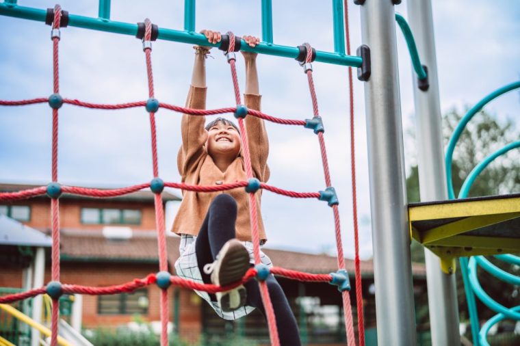 Happy young girl smiling while climbing a rope ladder at an outdoor playground. The image captures a moment of joy, strength, and confidence.