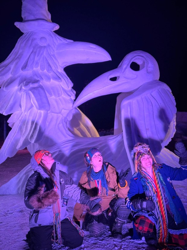 Three women in front of a snow sculpture.