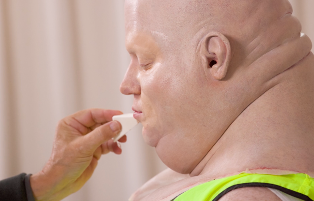 Still of Brennan Lee Mulligan having a giant baby head applied in the 'Last Looks' featurette for 'Very Important People' Season 3