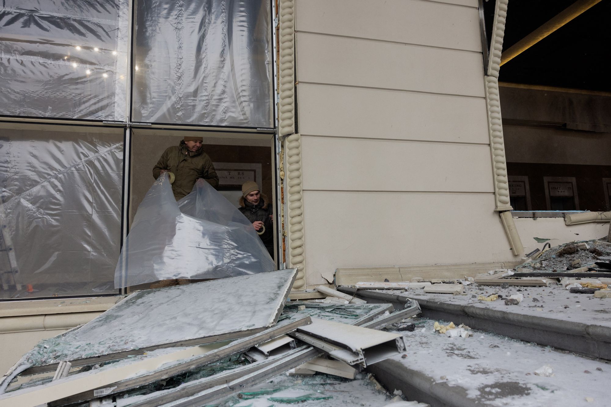 Men cover damaged windows with plastic sheeting following a Russian attack on a damaged residential complex in Kyiv on Friday