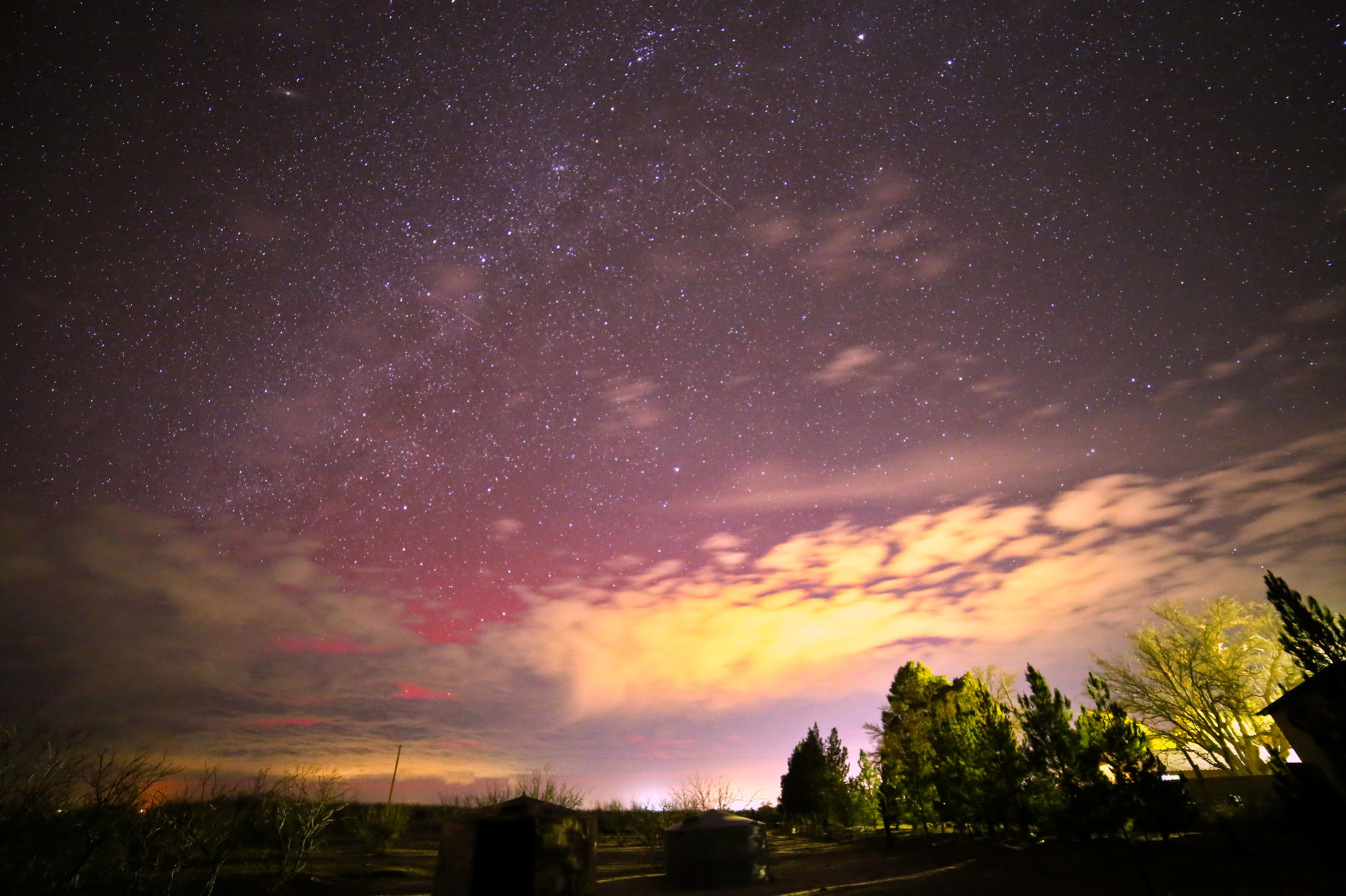 red northern lights against a starry sky with some clouds.