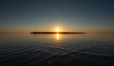 A sunset over a lake with a silhouette of an island right underneath the setting sun