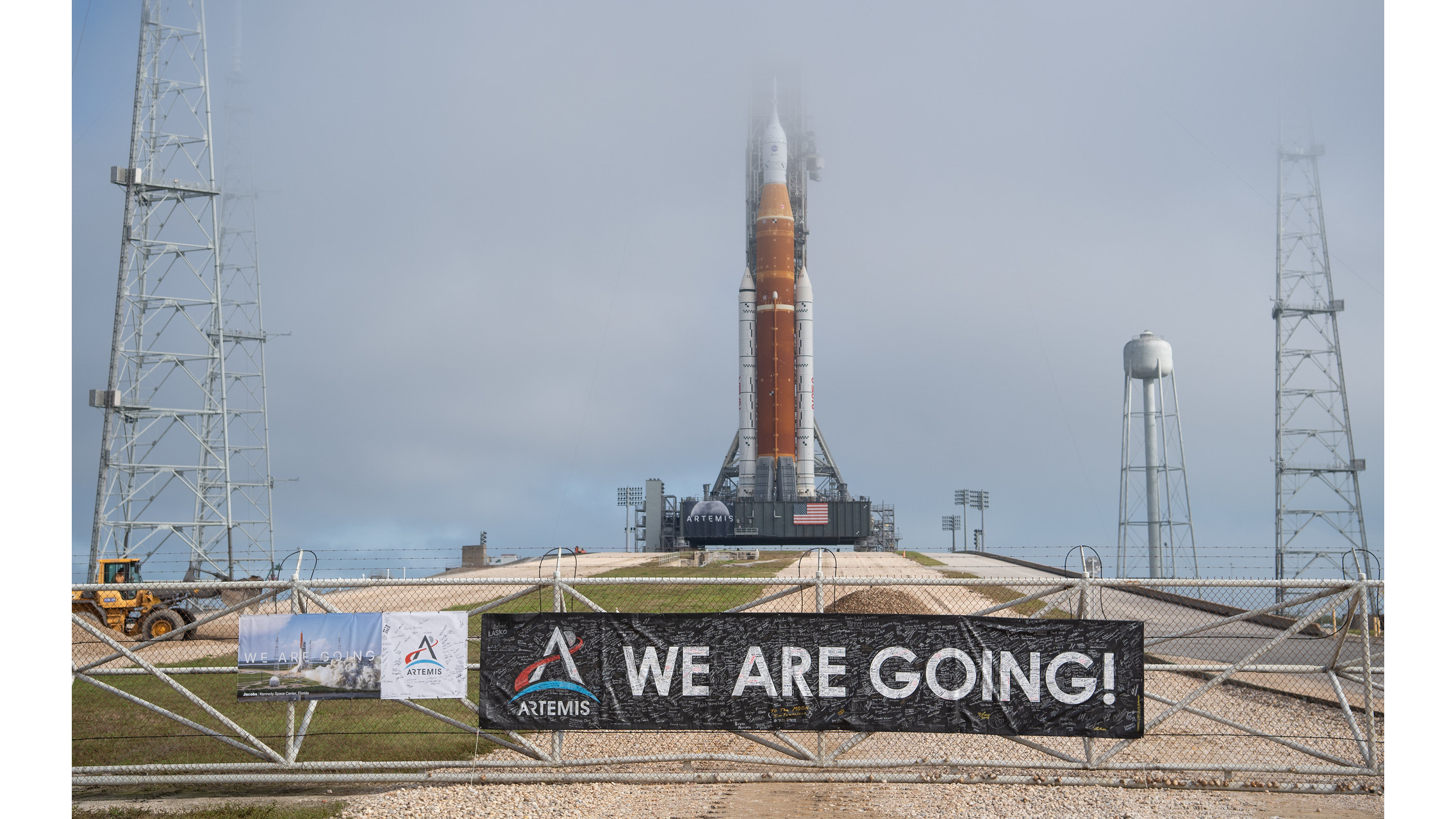 an orange and white rocket sits on a launch pad beneath cloudy skies