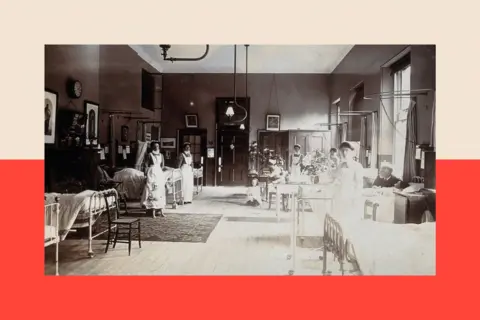 Heritage Images via Getty Images A black and white image of a ward at St Bartholomew's Hospital, London - beds are lined up either side of the room
