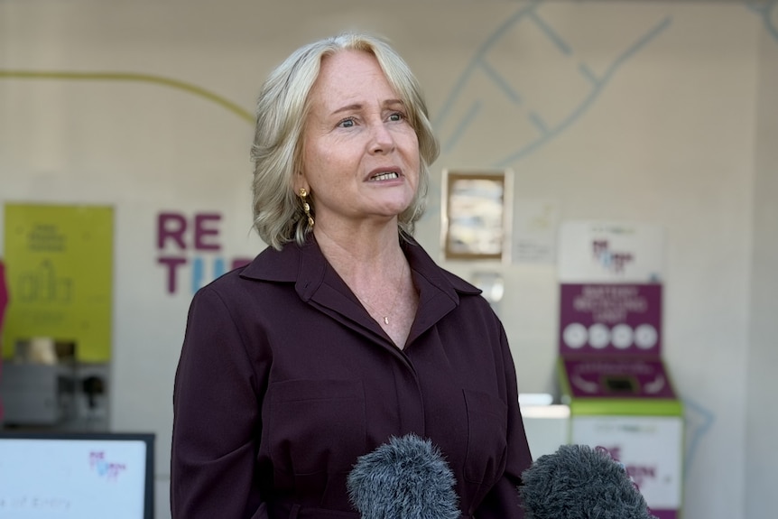 A woman in a maroon top speaking at a microphone.