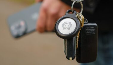 Apple AirTag on a keychain near someone holding an iPhone in the background.