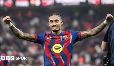 Raphinha, wearing a Barcelona shirt, spreads his arms wide in celebration