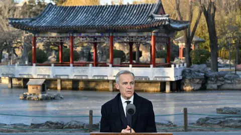Getty Images Canada's Prime Minister Mark Carney, wearing a suit and tie, speaks into a mike. Behind him is a structure with a traditional Chinese roofing style, with upturned eaves