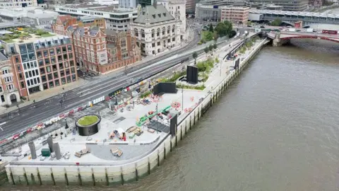 Tideway A large embankment going out onto a river. Trees, sculptures and seats are visible on it.