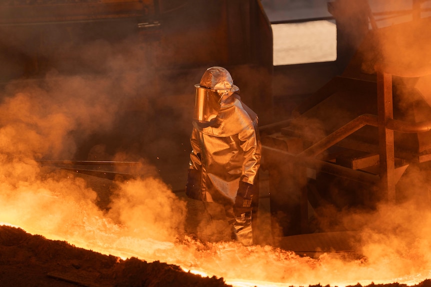 A steel worker in highly protective gear working on hot steel products.