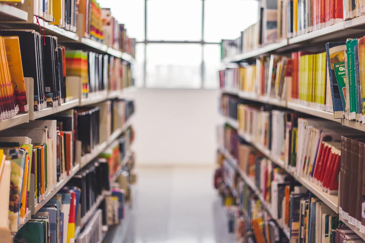 Looking down a row of books in a library with a blurred background of a clean, white floor, a white wall, and windows