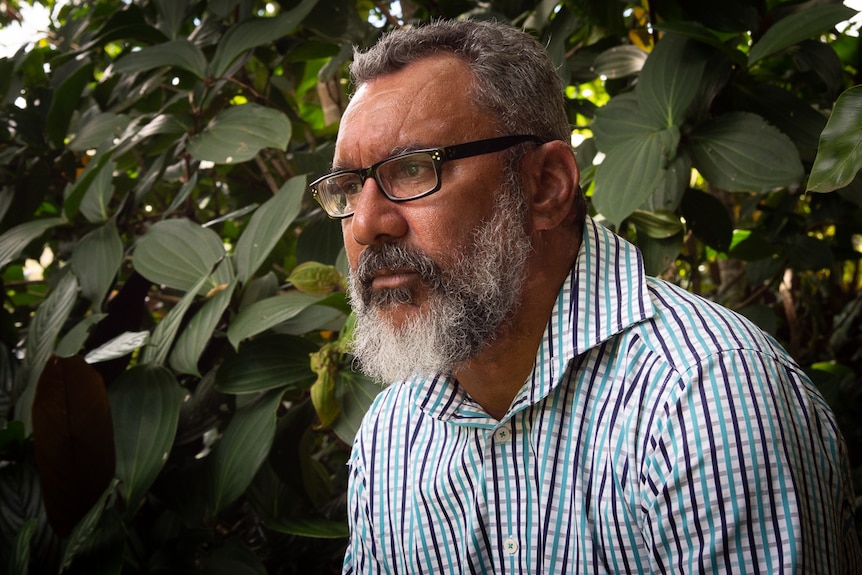Face of a bearded Torres Strait man in front of a bush.