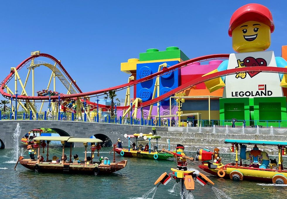 Colorful LEGOLAND with roller coaster, giant LEGO figure, and boats on a sunny day.