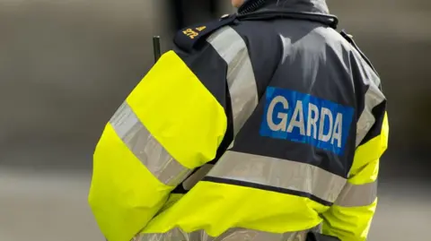 Getty Images The back of a gardaí uniform raincoat. Garda is written in white and blue, and the rest of the coat is a reflective neon yellow colour with silver stripes on the arms and chest area.