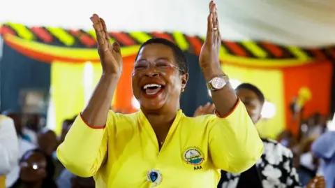 Reuters A woman in a bright yellow top lifts her hands up in joy as she celebrates the election victory.