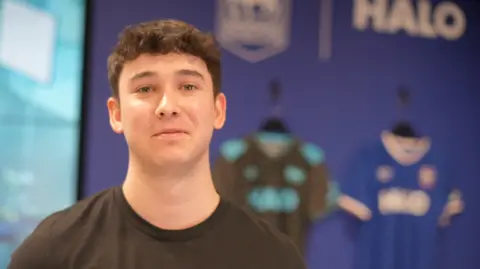 Jamie Niblock/BBC Dan Sheridan in an office. He has short dark hair, slightly curly at the forehead and is wearing a black T-shirt.