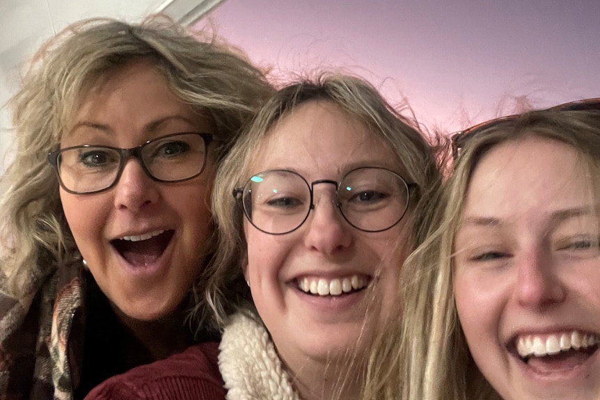 A selfie of a middle aged woman with two young women. They're all smiling
