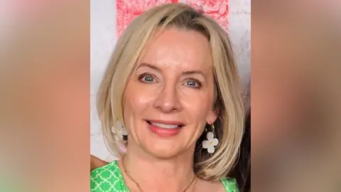 Sam Phipps Sam Phipps smiles while wearing a green dress, necklace and flowery earrings. She has blond hair