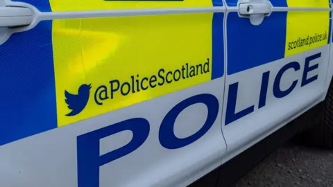 Getty Images The close up of the side of a Police Scotland car. It has the word "police" and Police Scotland's Twitter/X and website addresses.