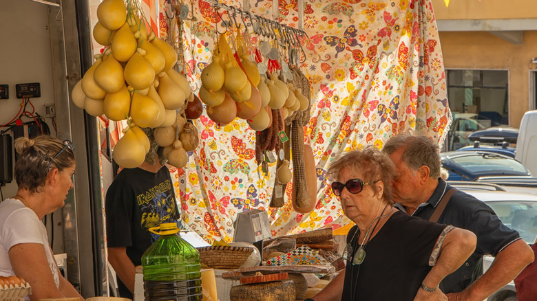 Elder locals gather at a cheese and ham market stall in Arzachena, Sardinia