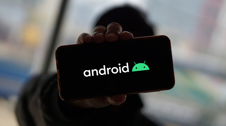 Person holding up a smartphone with the Android logo displayed on screen
