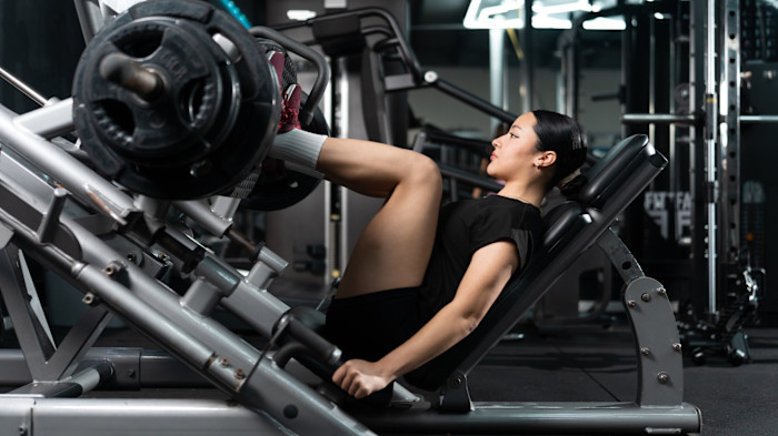 A young woman in athletic wear using a leg press machine, appearing focused while lifting weights in a modern gym.