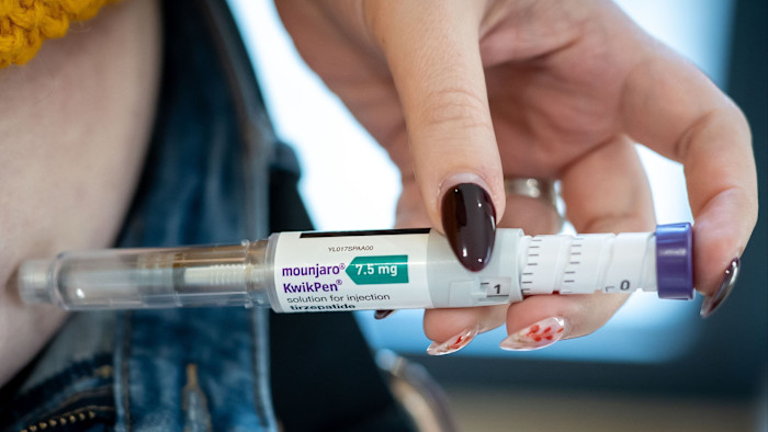 A hand holds a Mounjaro KwikPen injection pen, labeled 7.5 mg tirzepatide, pressed against bare skin.