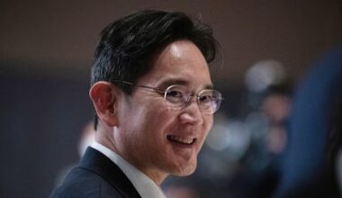 Samsung chair Lee Jae-yong smiling and wearing glasses at an event, with blurred attendees in the background.