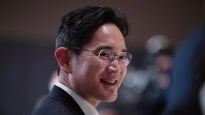 Samsung chair Lee Jae-yong smiling and wearing glasses at an event, with blurred attendees in the background.