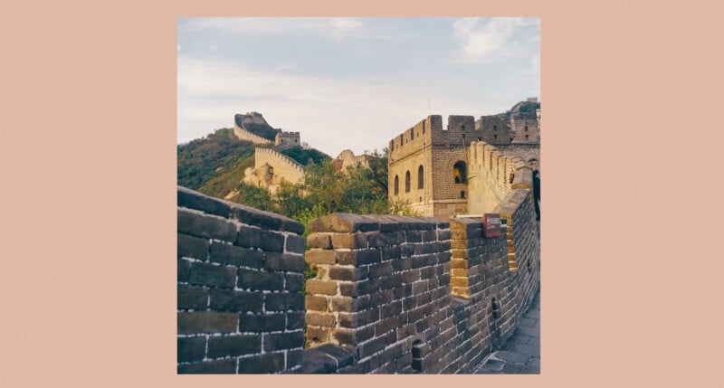 A section of the Great Wall of China winds over green hills under a partly cloudy sky, with stone towers and brick walls prominent in the foreground.