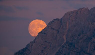 a large supermoon is partially hidden by a rocky mountain, the moon appears large and slightly orange.