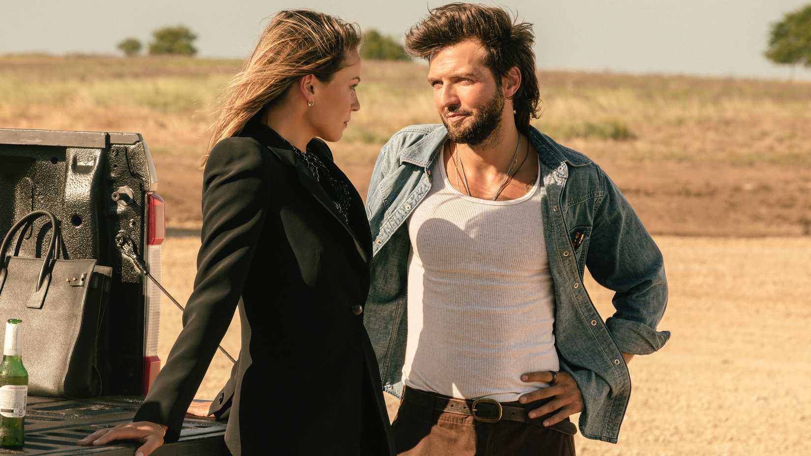 Kayla Wallace's Rebecca and Guy Burnet's Charlie leaning against a truck flirting with each other in Landman season 2