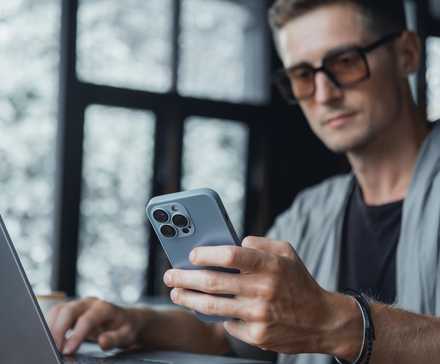 man holding iphone while looking at laptop