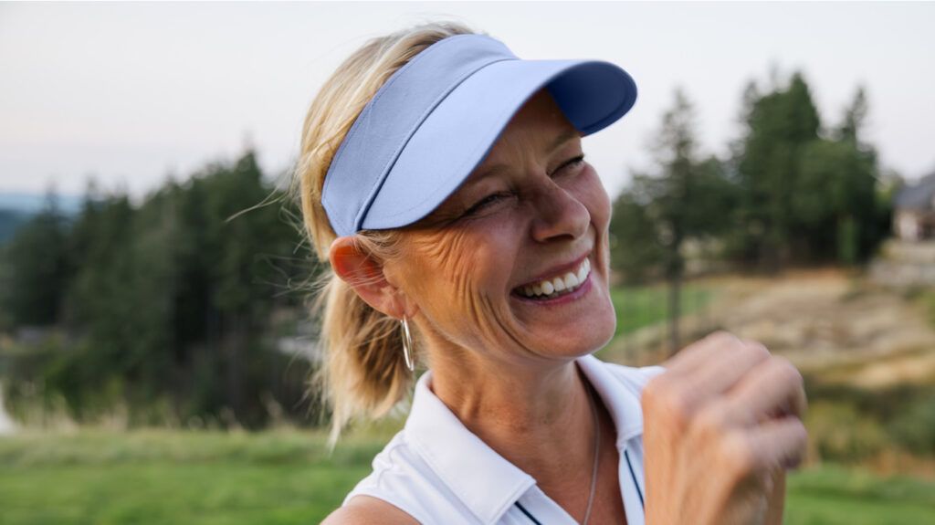 An older woman wearing a tennis cap and outfit smiles