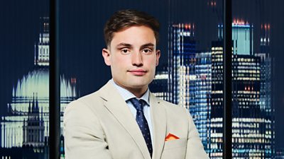 A man in a beige suit looks on outside a city backdrop