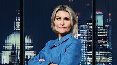A woman in a smart blue shirt stands in front of a city backdrop at night 