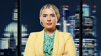 A woman in a cheerful yellow suit stands outside a city landscape at night